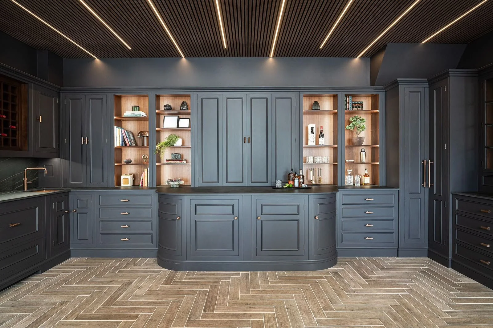 After: the same room with navy cabinetry, lit display shelves and a herringbone floor