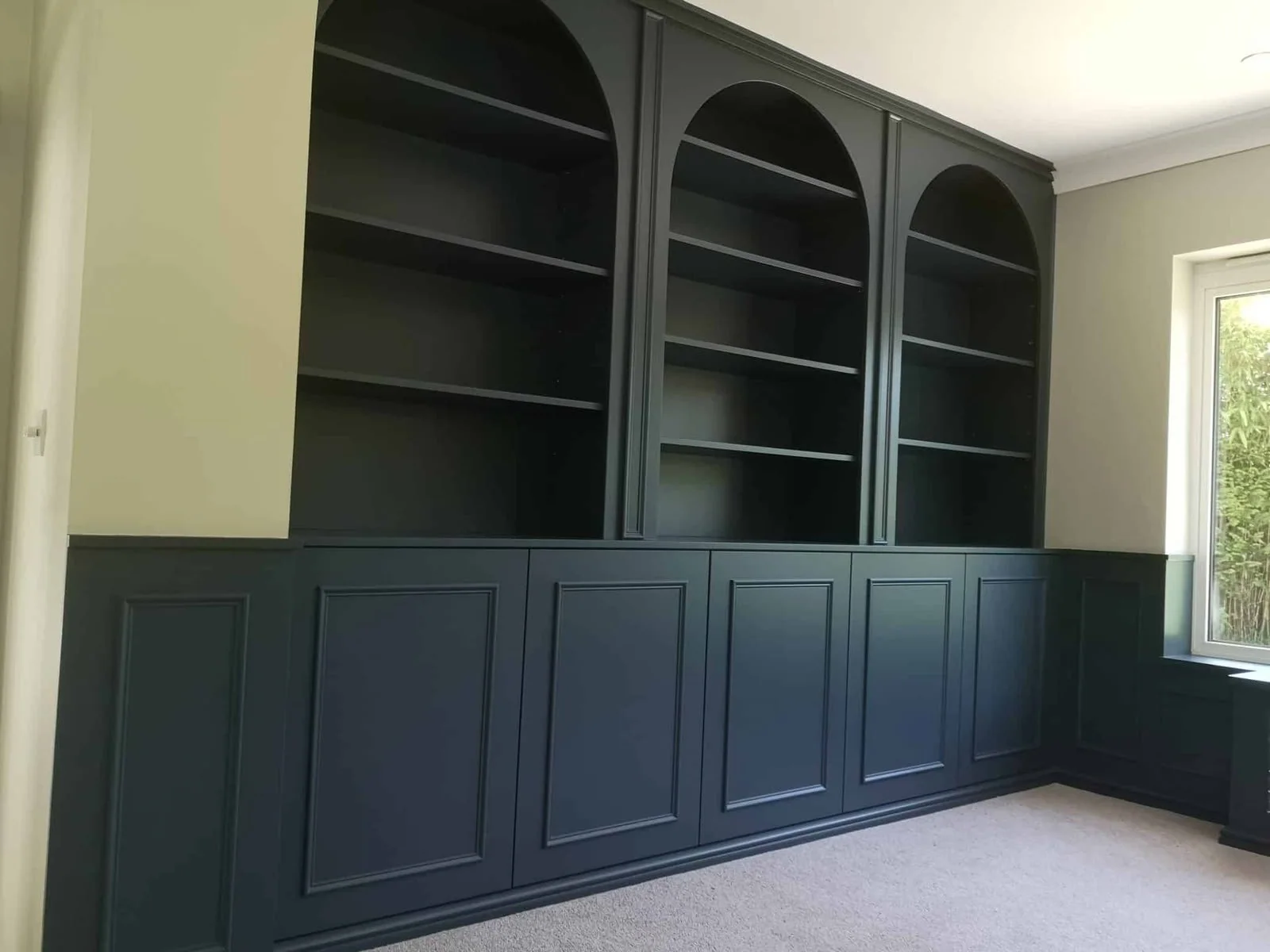 Built-in arched bookcases over panelled cupboards, painted navy